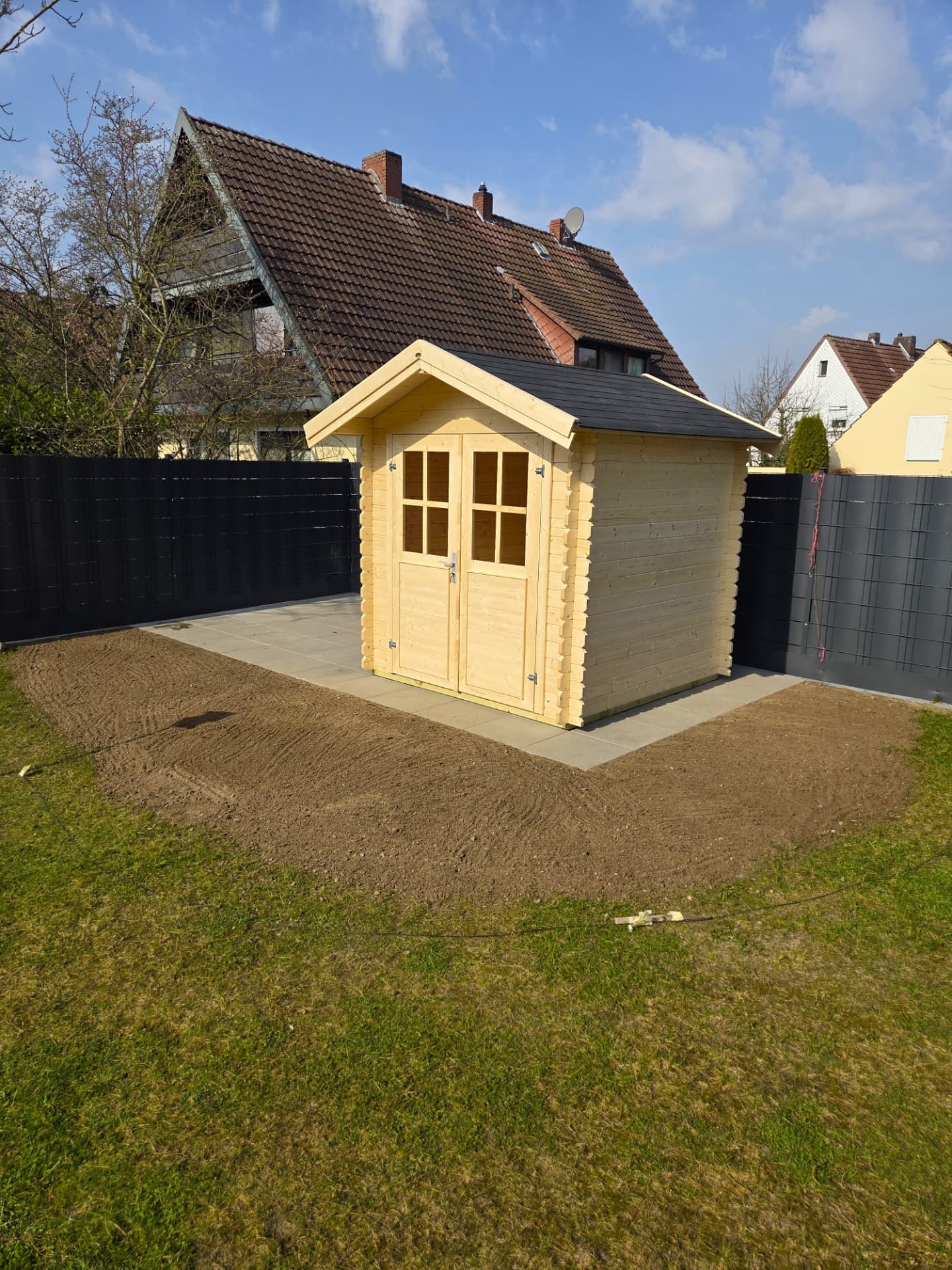 Gartenhüttenaufbau fertig: fertige Blockbohlenhütte auf dem gepflasterten Fundament